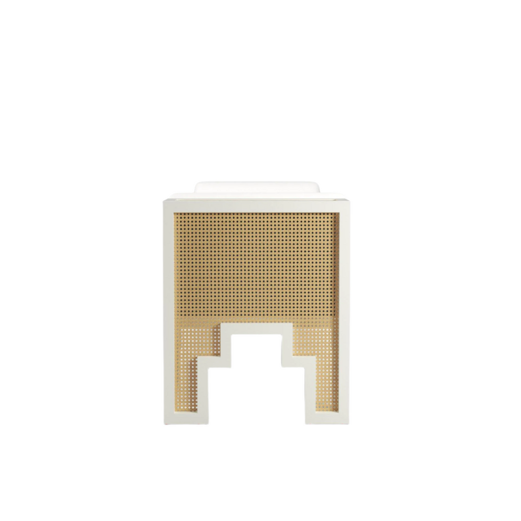 Front-facing view of a natural rattan cane panel set in a white painted solid wood frame with a stepped geometric cutout at the base, topped by a white upholstered cushion for an end-of-bed bench.