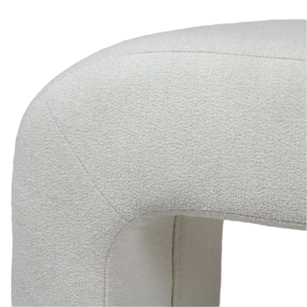 Close-up of the bench's curved end showing cream boucle upholstery with visible seam and textured looped fabric on an armless, back-of-bed seating piece.