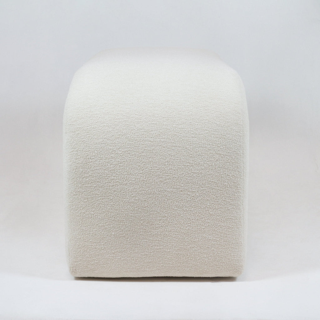 Front view of a backless end-of-bed bench upholstered in cream boucle fabric, showing rounded corners and a low, minimalist coastal-modern silhouette on a white background.