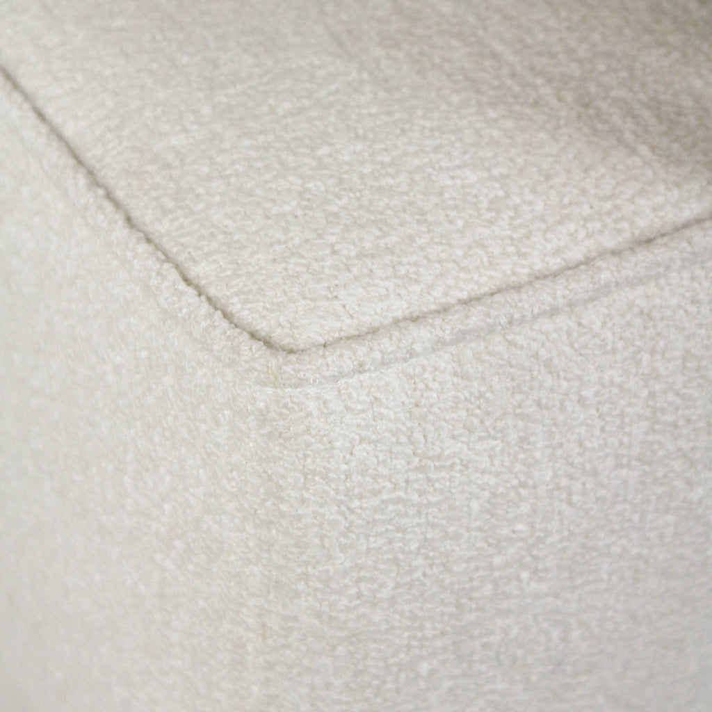 Close-up of a white boucle upholstered bench corner showing the piped edge and textured looped fabric.