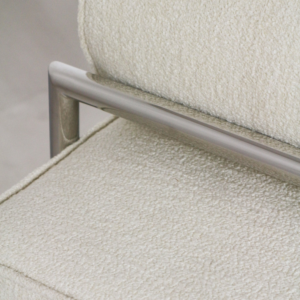 Close-up of a white boucle-upholstered seat and back cushion with a brushed stainless steel frame bar, highlighting the textured fabric and seam detail on a modern end-of-bed bench.