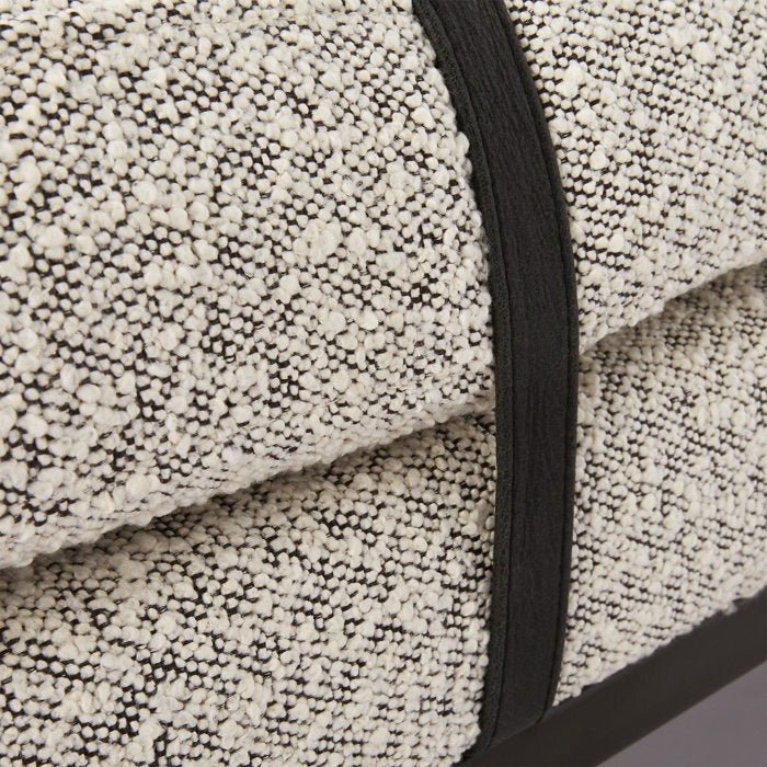 Close-up of natural cream boucle upholstery on a bench showing looped textured fabric, contrasting black trim strap and a dark wood base edge.
