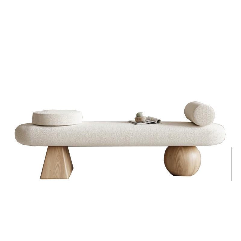 75-inch off-white boucle-upholstered end-of-bed bench with natural wood legs — one tapered geometric leg and one spherical leg — styled with a round bolster, a circular cushion and a small magazine on top.
