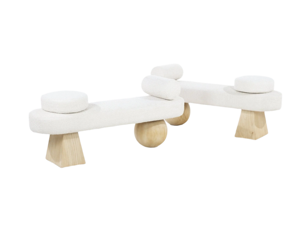 75-inch white boucle upholstered end-of-bed bench with sculptural natural wood legs (tapered block and round supports), topped with round removable cushions and cylindrical bolsters in a modern coastal style.
