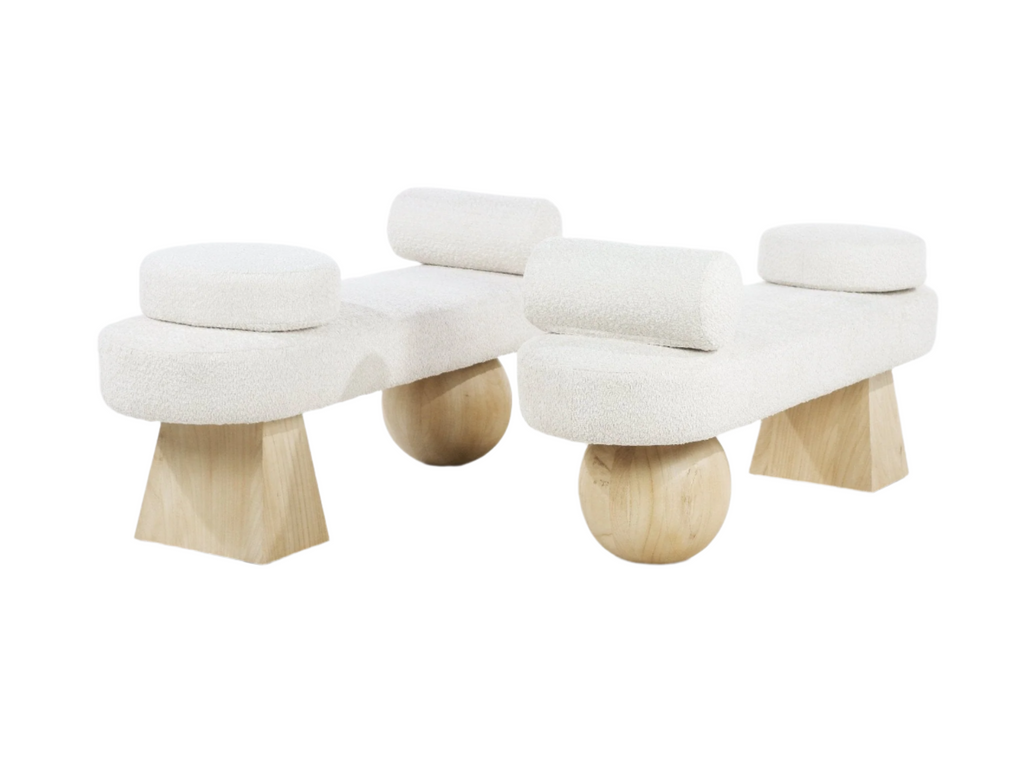 Pair of cream boucle-upholstered end-of-bed benches with round bolster cushions, each supported by natural light wood ball and trapezoid legs in a modern coastal style on a white background.