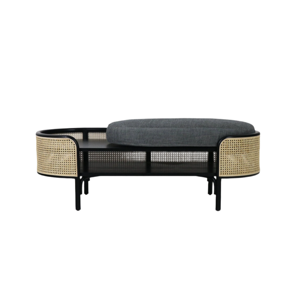Boho-style low bench with a black solid wood frame, curved natural rattan cane panels and a thick gray upholstered cushion sitting over a slatted shelf, ideal for bedroom or entryway seating.