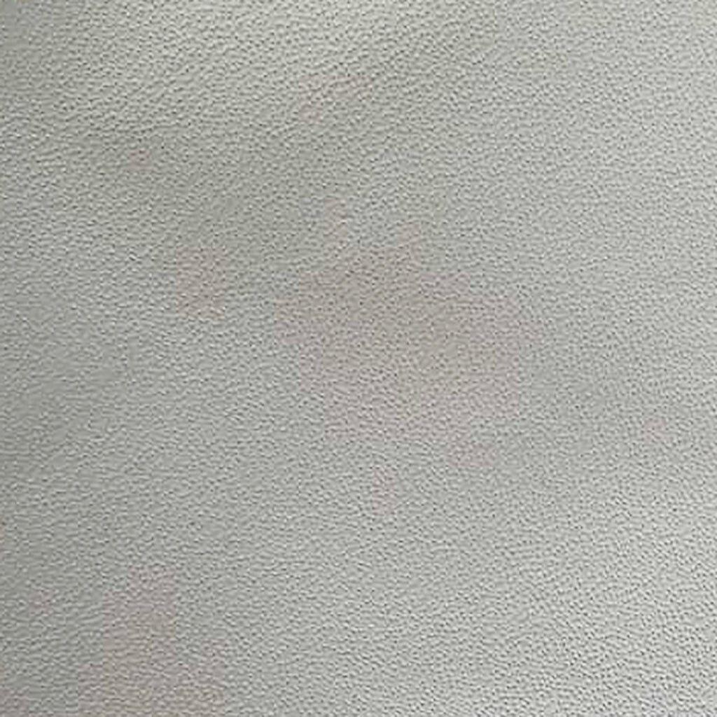 Close-up of cream leather dining chair upholstery showing pebble-grain texture with subtle pinkish discoloration spots on the surface.