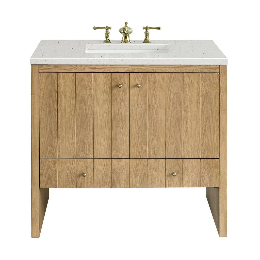 Freestanding 36-inch single-sink bathroom vanity in light natural oak with vertical plank doors, white speckled stone countertop and rectangular undermount sink, fitted with polished brass widespread faucet and round brass knobs.