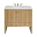 Freestanding 36-inch single-sink bathroom vanity in light natural oak with vertical plank doors, white speckled stone countertop and rectangular undermount sink, fitted with polished brass widespread faucet and round brass knobs.