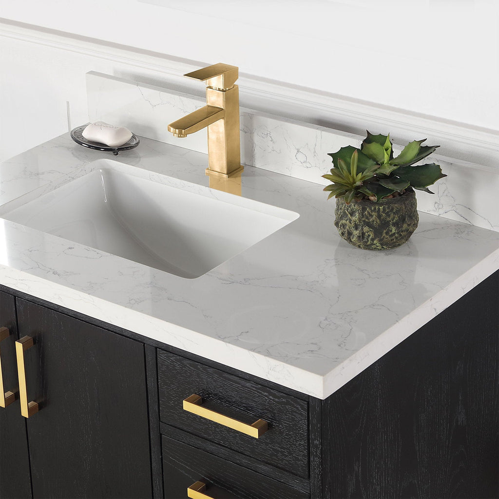Modern black solid wood vanity with white stone top and subtle gray veining, integrated ceramic sink, gold brass faucet and matching brass handles; small potted succulent and soap dish on the counter.