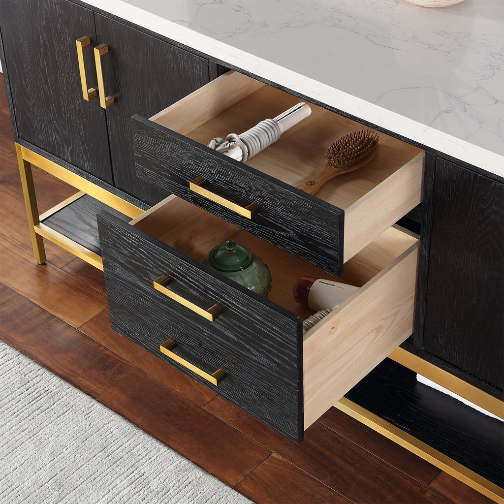 Close-up of a modern solid-wood bathroom vanity with a white stone countertop, black wood-grain drawer fronts and gold metal handles and base; two open drawers show natural wood interiors with a hairbrush, curling iron and jar.