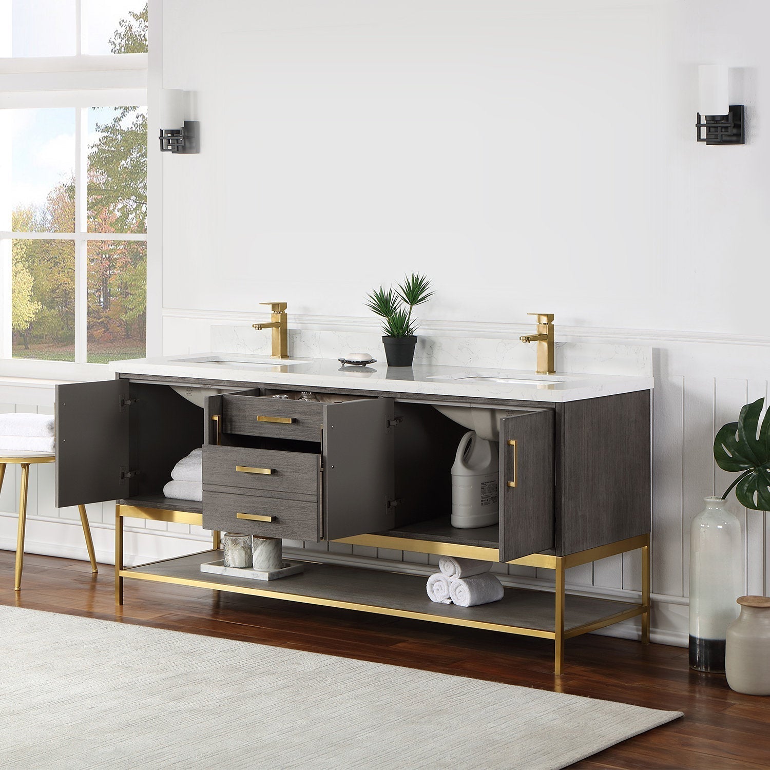 Modern solid wood 72-inch double-sink vanity in stone finish with white stone countertop, gold faucets and gold metal base; open cabinets reveal central drawers, lower shelf storage and rolled towels.