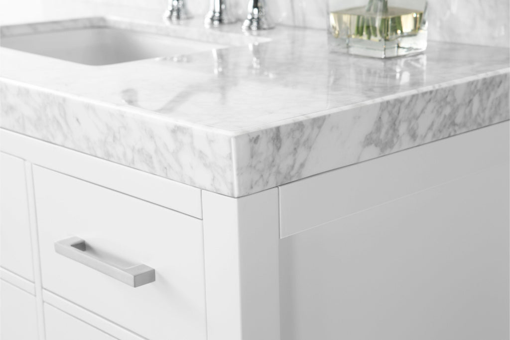 Close-up of a white solid wood bathroom vanity corner with a thick white marble stone top with gray veining, undermount sink and chrome faucet reflection, and a brushed metal rectangular drawer pull.