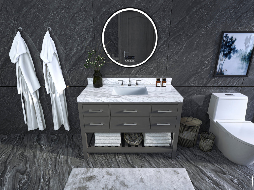 48-inch stone-colored solid wood freestanding vanity with white marble top and undermount ceramic sink, chrome faucet, round LED mirror, open towel shelf and dark stone tile walls.