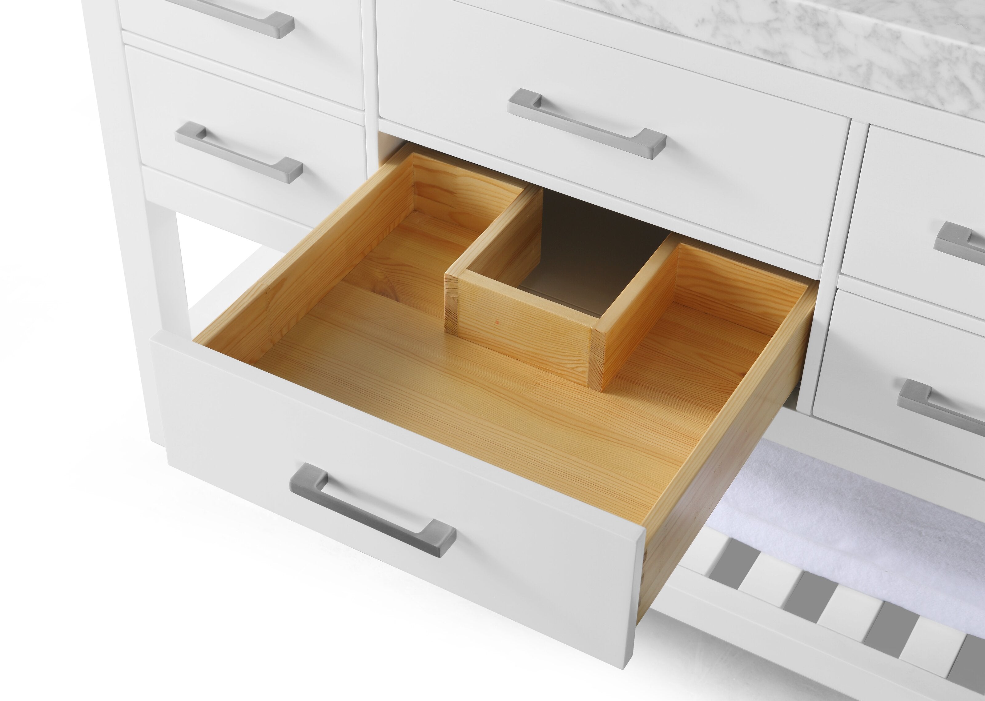 Open drawer of a white modern bathroom vanity revealing a natural solid wood interior with a center divider, marble stone countertop edge, gray metal handles and a lower slatted shelf with towel visible.