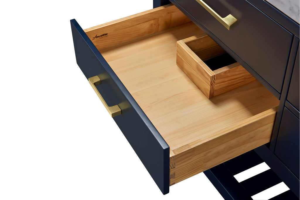 Close-up of an open navy bathroom vanity drawer revealing a natural solid wood interior with dovetail joints and a small wooden organizer, shown with a brushed gold rectangular drawer handle.