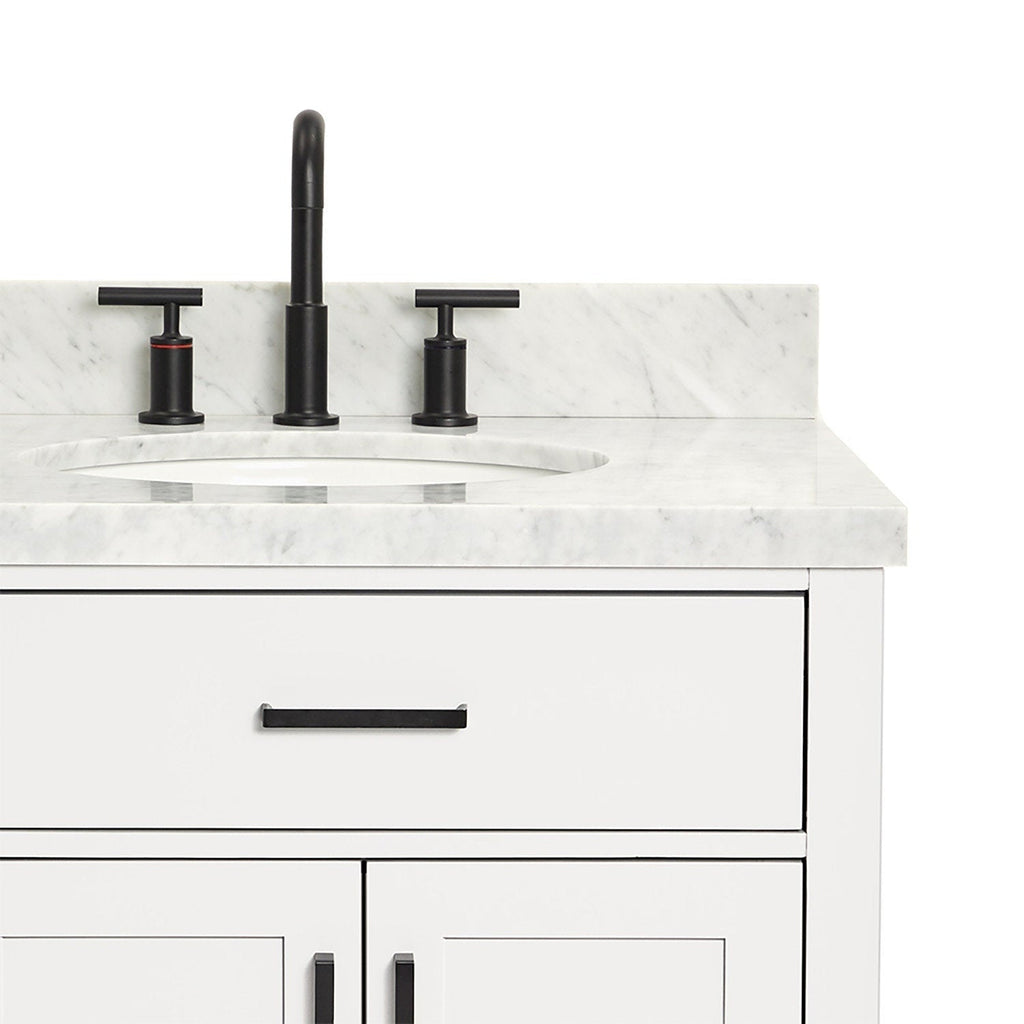 Close-up of a white wooden bathroom vanity with a stone marble top and backsplash, oval undermount sink, matte black three-piece faucet, and matching black drawer and door handles.