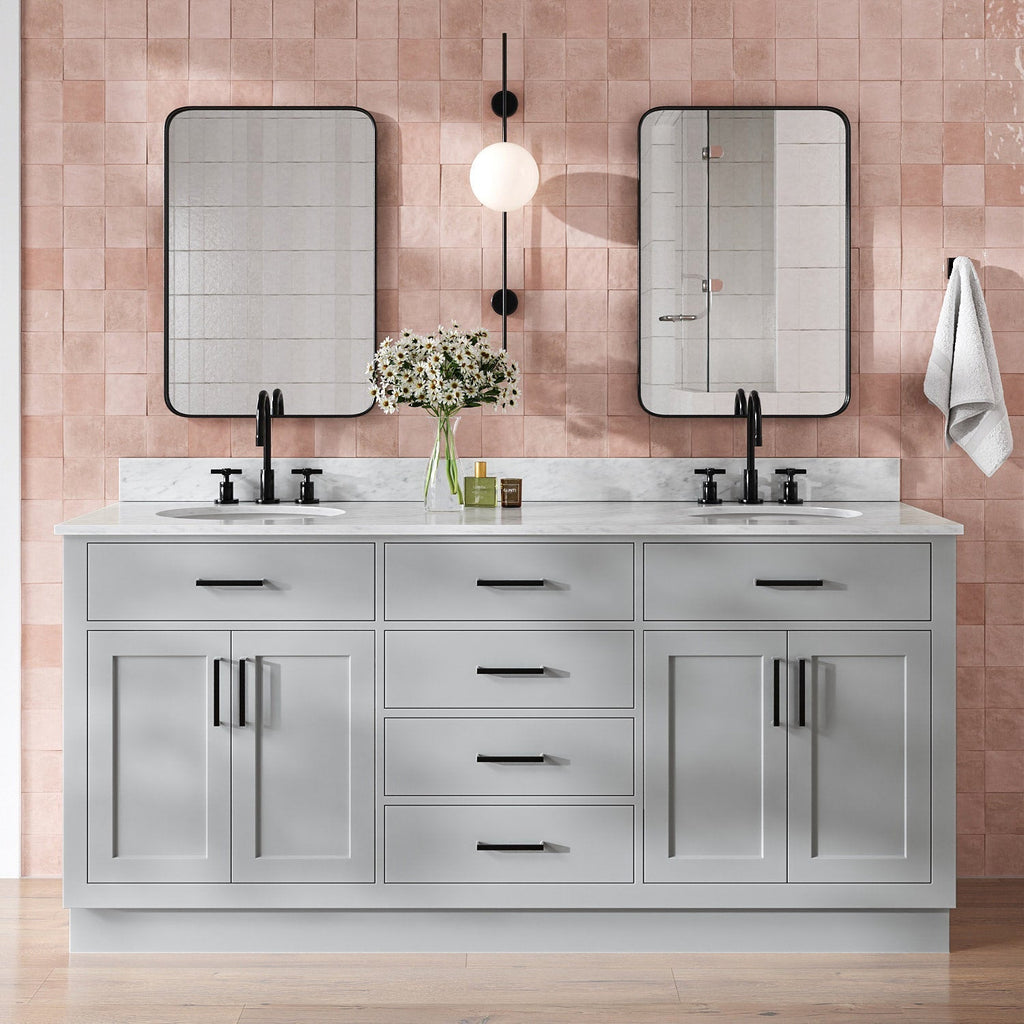 73-inch gray solid wood double-sink bathroom vanity with Giotto quartz countertop, two undermount white ceramic sinks, matte black faucets and hardware, black-framed mirrors, central globe wall sconce, vase of daisies and pink tile backsplash.