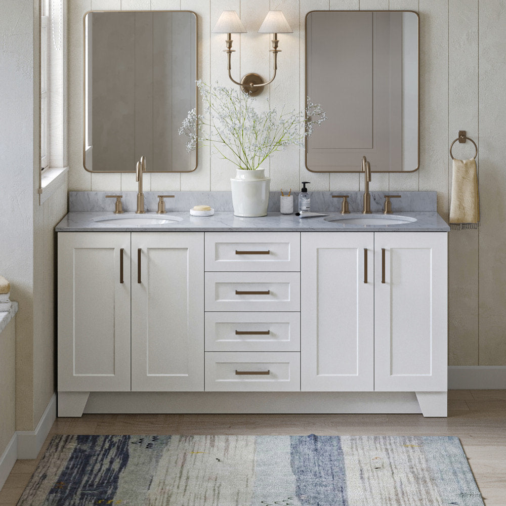 Modern solid-wood 73-inch double-sink bathroom vanity with gray stone countertop, white shaker cabinets and central drawers, satin bronze faucets and hardware, two rectangular mirrors, wall sconce and ceramic vase with flowers.