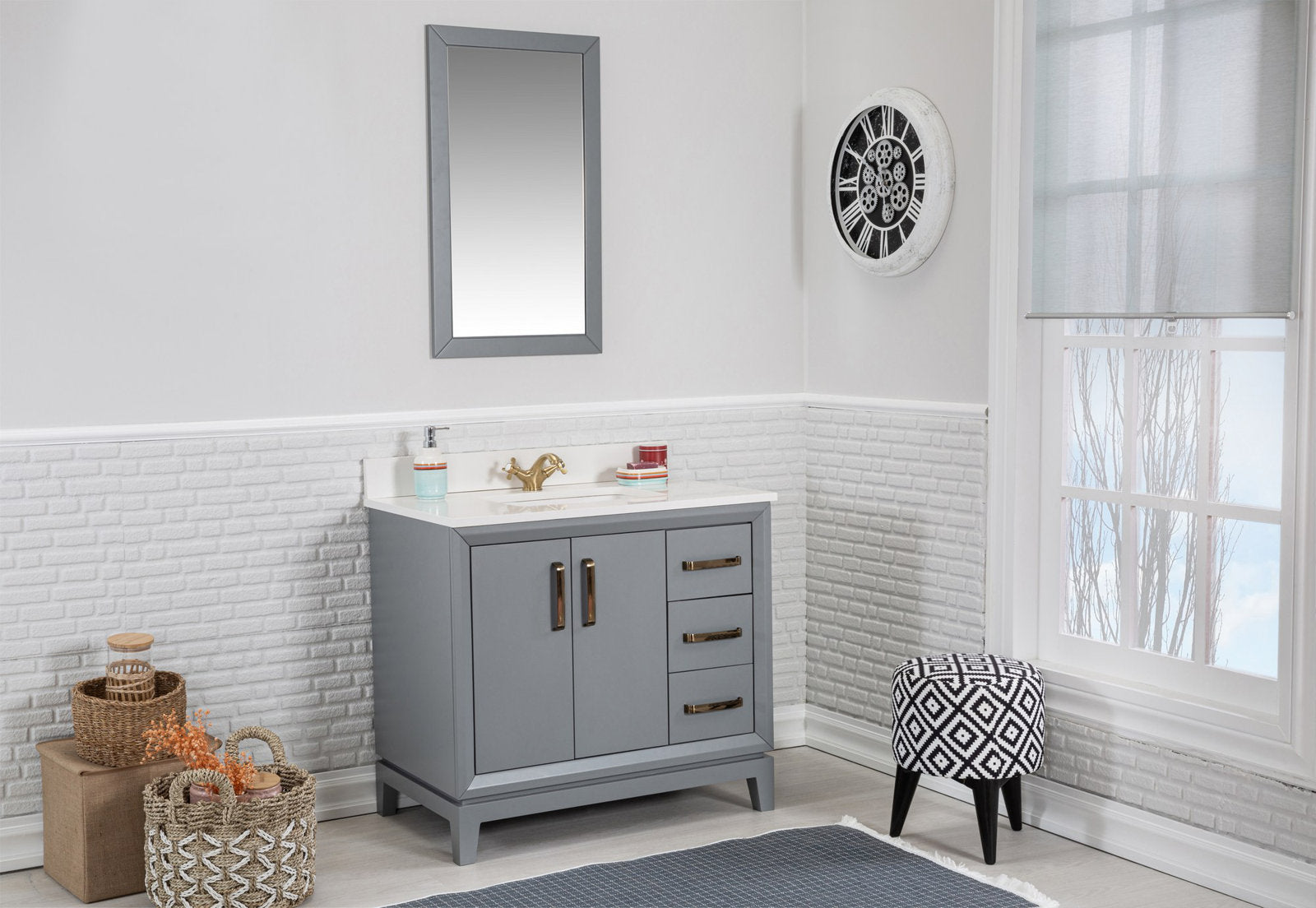 Freestanding modern gray solid wood bathroom vanity with white stone countertop and brass faucet, two doors and three drawers; rectangular mirror above, woven storage baskets to the left and a black-and-white patterned stool by the window.