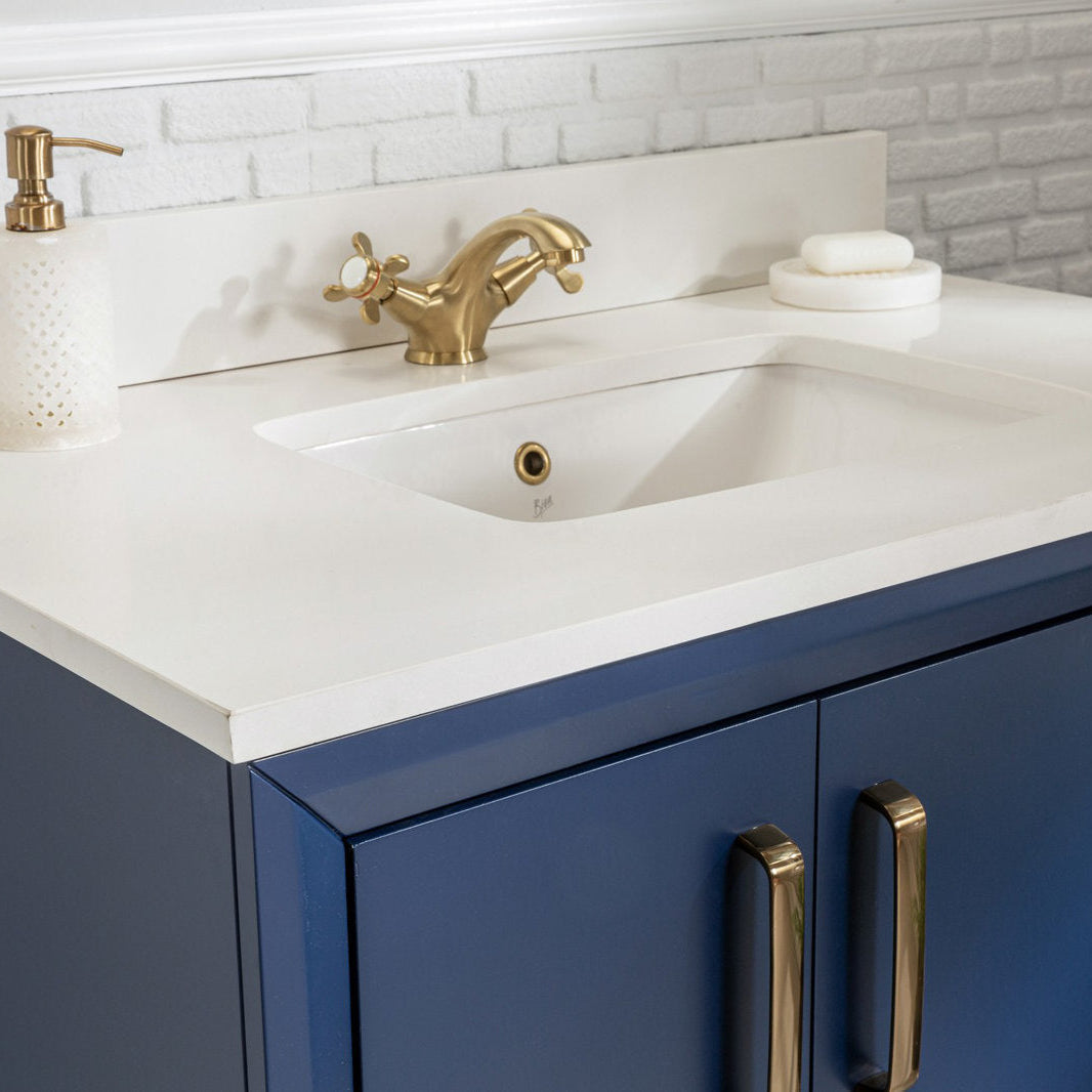 Close-up of a modern navy blue solid wood vanity with a stone white countertop and integrated rectangular sink, brass faucet and matching brass handles, plus a soap dispenser and soap dish against a white textured backsplash.