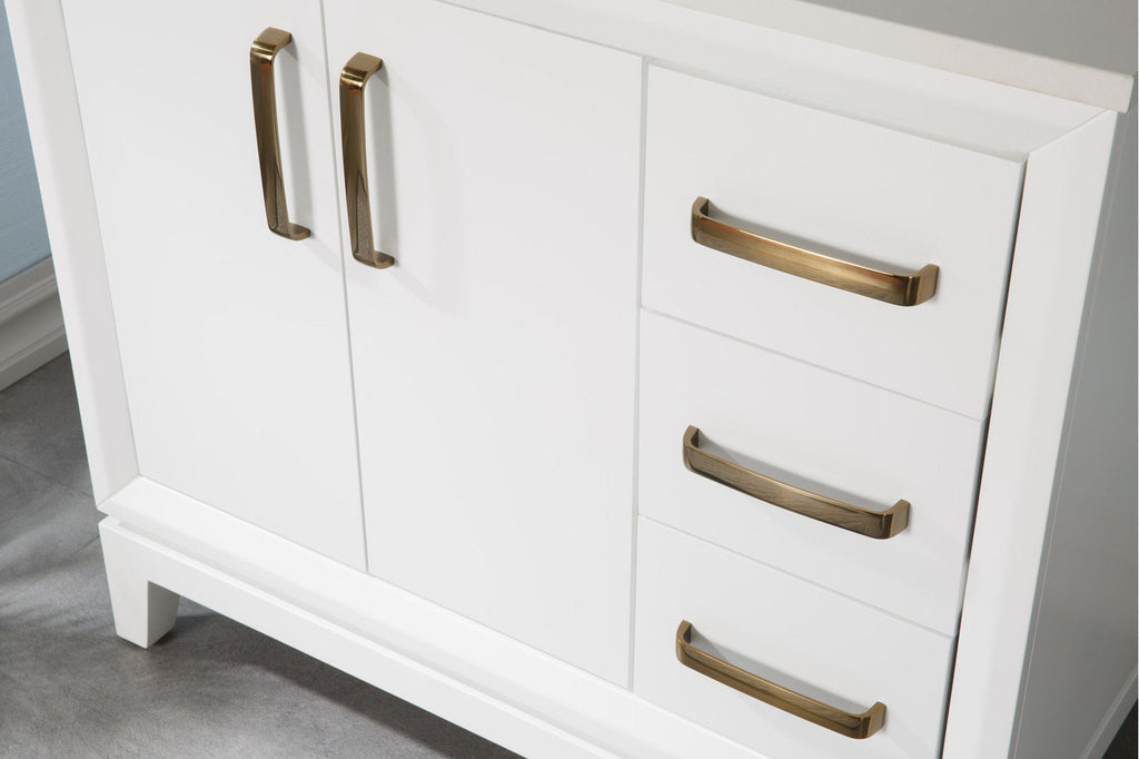 Close-up of a modern white solid wood bathroom vanity with a stone countertop edge and brushed brass drawer and door pulls, showing two cabinet doors and three drawers with matching metallic handles.