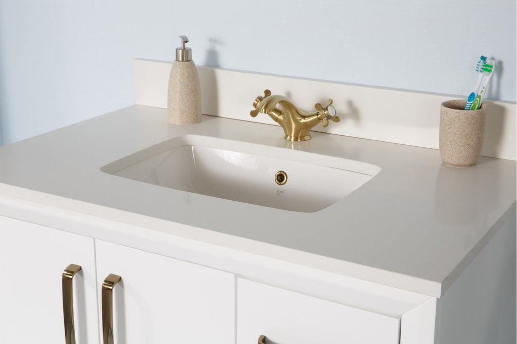 Modern white solid-wood vanity with a stone-colored countertop and integrated white ceramic undermount sink, gold double-handle faucet and matching gold cabinet pulls, with stone-look soap dispenser and toothbrush cup on top.