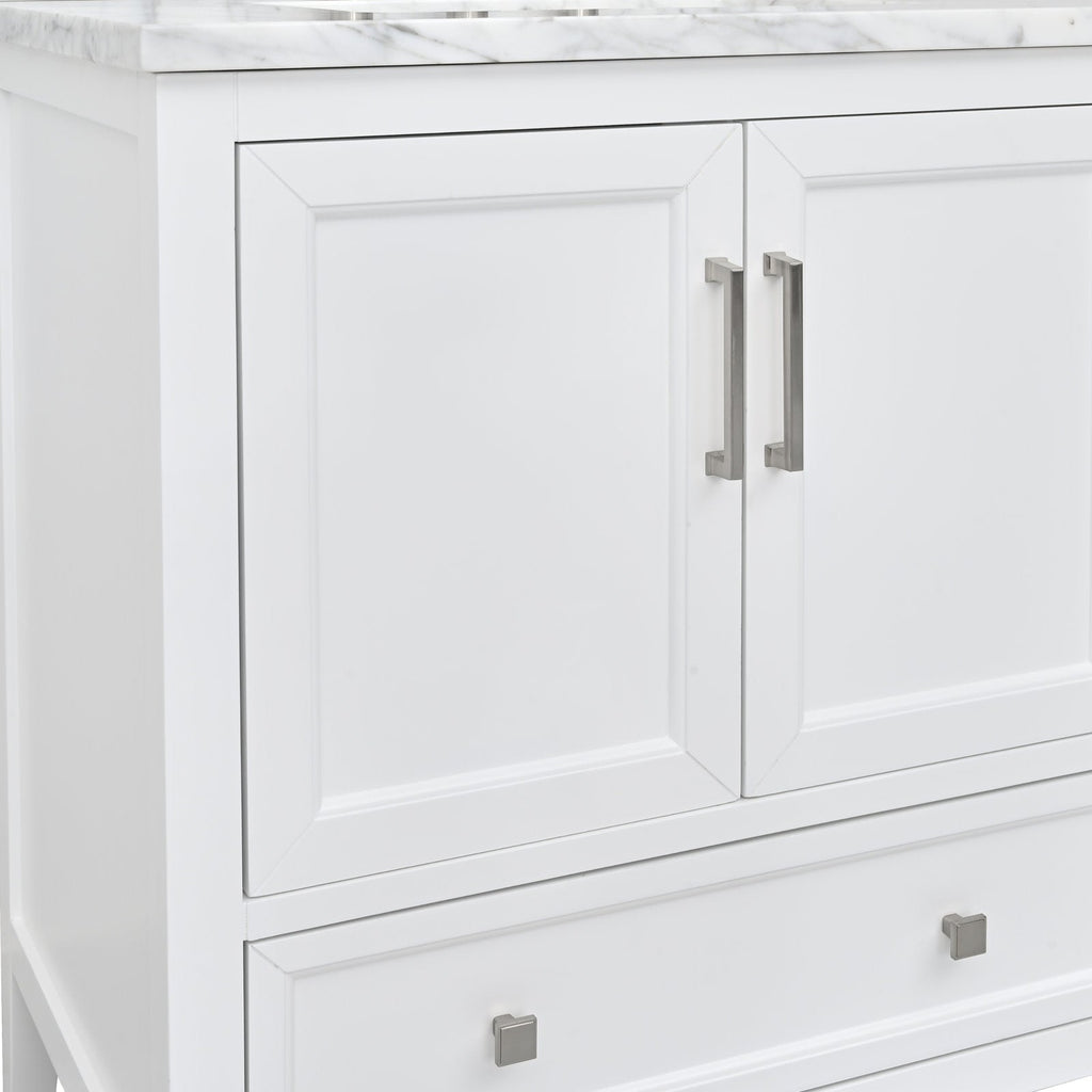Close-up of a stone-topped modern white solid wood bathroom vanity showing two inset paneled doors with brushed nickel bar handles and a lower drawer with square metal knobs.