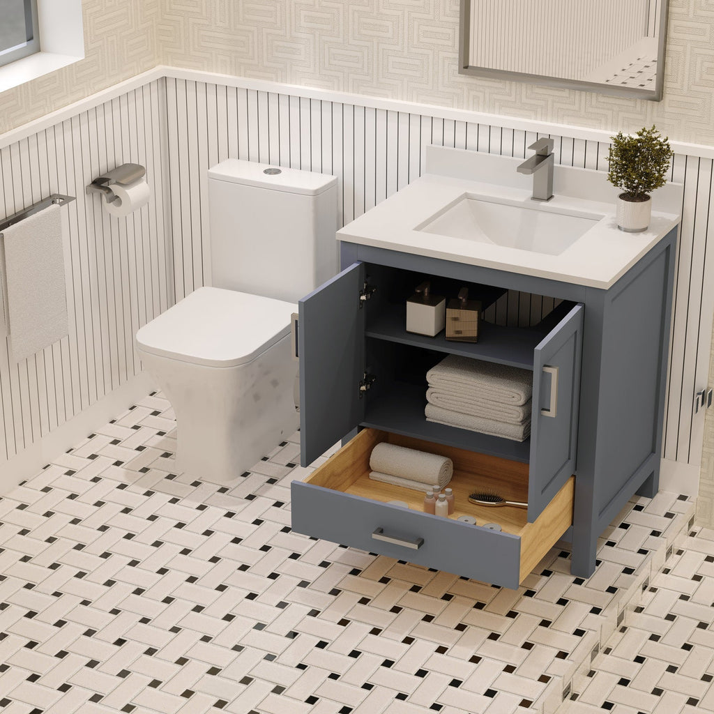 Modern 30-inch freestanding solid wood bathroom vanity in a gray-blue finish with a white stone countertop and integrated sink; open cabinet and wood-lined bottom drawer holding folded towels and toiletries beside a toilet.