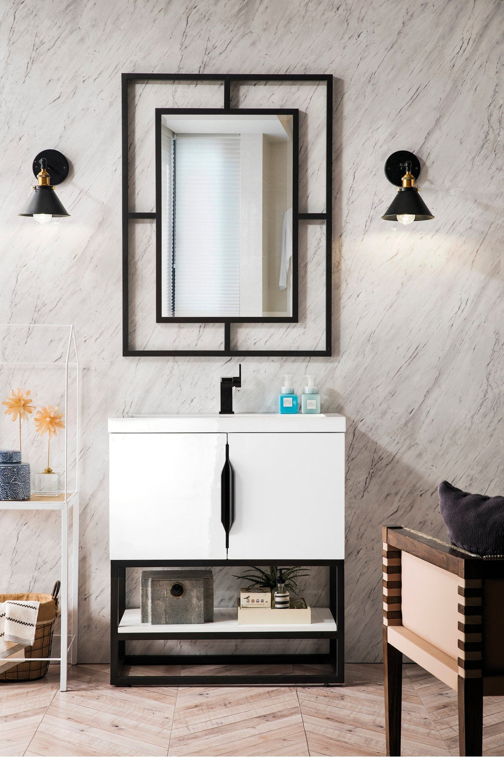 Modern white single-sink solid-wood vanity with a stone top, black single-handle faucet and vertical black handle, open black base shelf with decor, geometric black-framed mirror and two black-and-brass wall sconces on a marble-look wall.