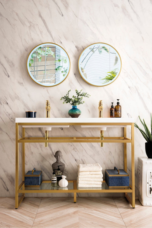 Freestanding glam-style double bathroom vanity with a gold metal frame and white stone top, two ceramic under-mount sinks and gold faucets, paired with round gold-framed mirrors and an open lower shelf styled with towels and accessories.