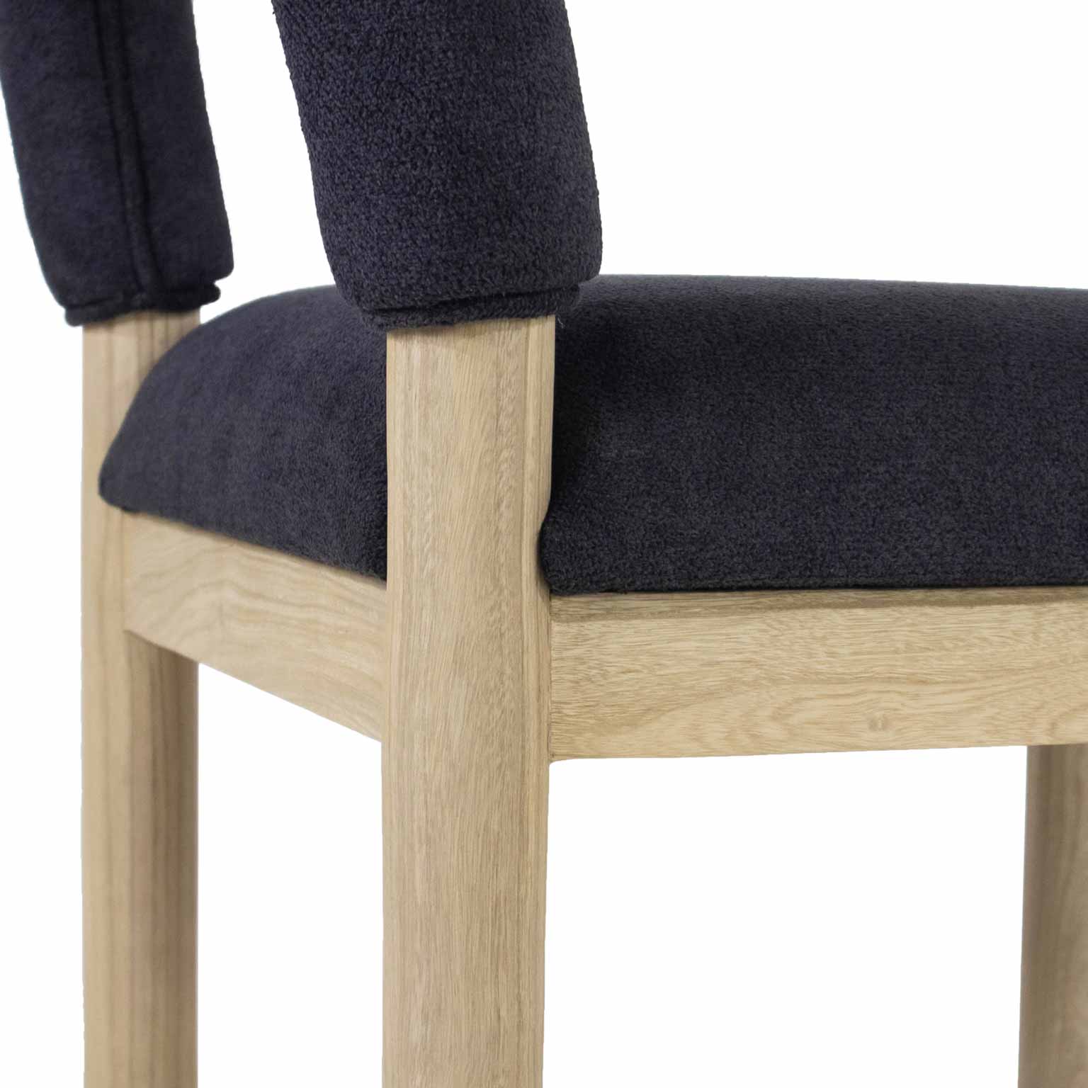 Close-up of a charcoal bouclé upholstered seat and low back on a light oak stool frame, highlighting the textured fabric and natural oak grain.