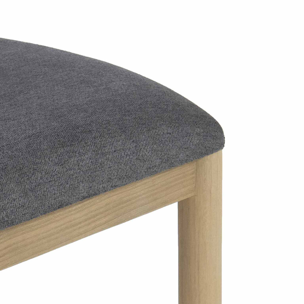 Close-up of a gray boucle upholstered seat cushion on a natural oak stool frame and rounded leg, highlighting the fabric texture and light wood grain.