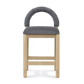 Front view of a counter stool with natural oak frame, cushioned dark gray boucle seat and rounded low back, photographed against a white background.