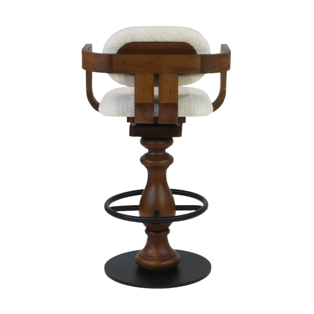 Rear view of a swivel bar stool with light beige fabric upholstery, curved teak wood back and seat frame, turned teak pedestal, black metal ring footrest and round black metal base.