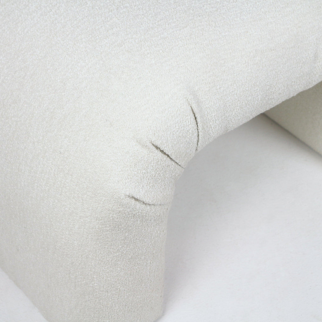 Close-up of a cream boucle upholstered vanity bench corner showing the curved arch detail, looped textured fabric and visible stitched seams.