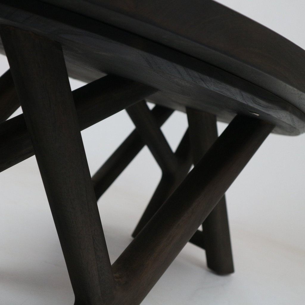 Close-up of the underside of a modern mahogany coffee table in a smoked-black finish, showing solid wood crossed legs and the rounded tabletop edge.