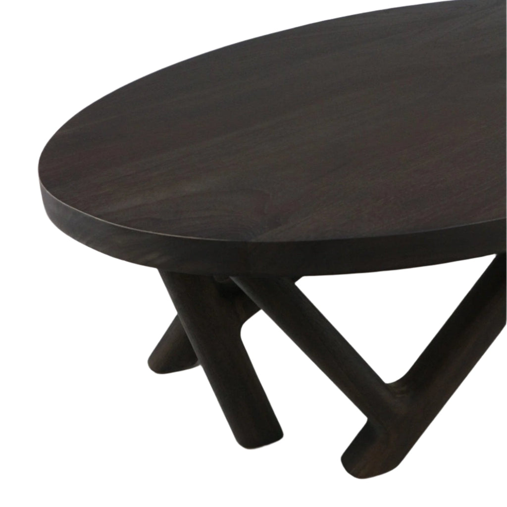 Close-up of a round solid-wood mahogany coffee table top in a smoked-black finish, showing intersecting angled legs and the table edge in a modern contemporary style.