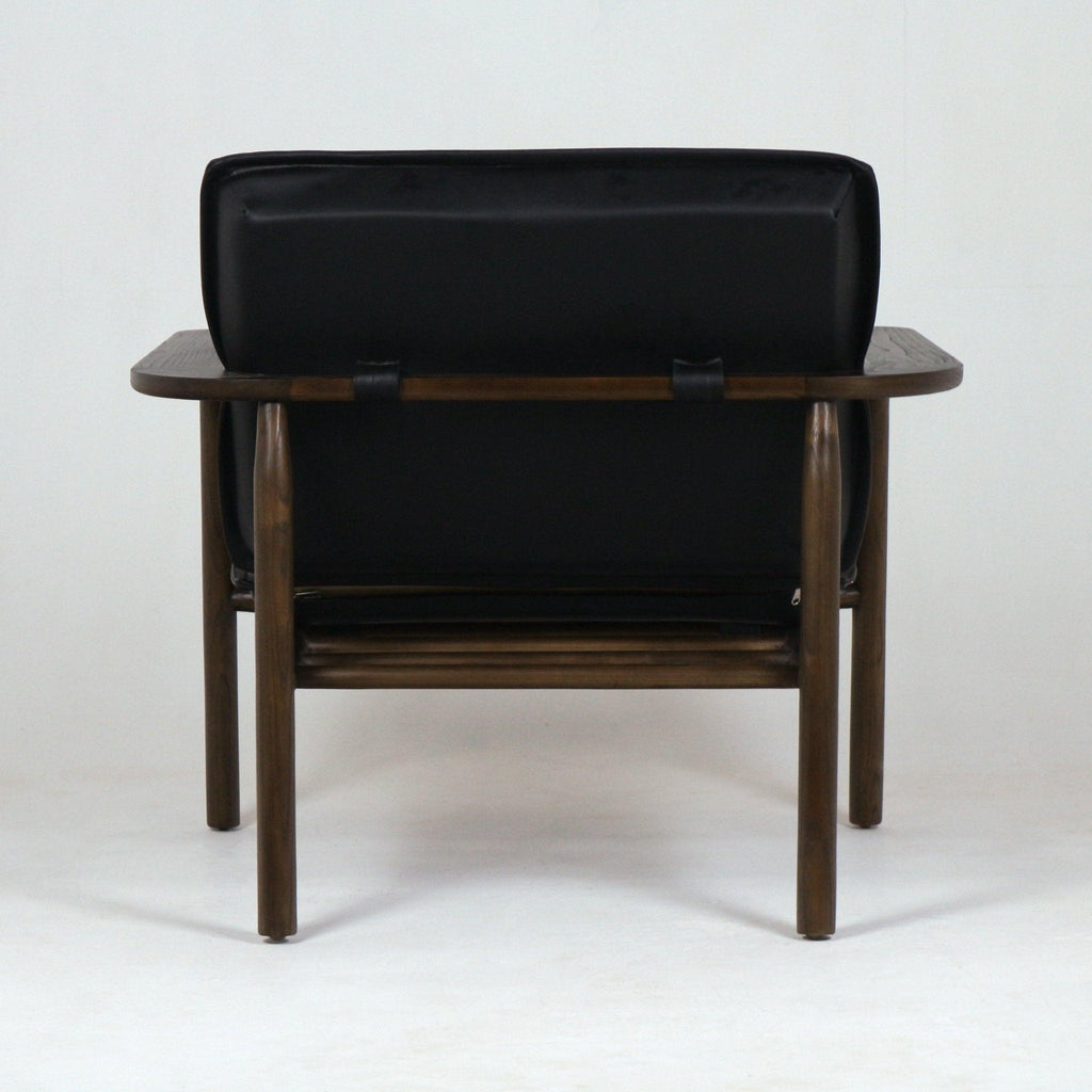 Rear view of a mid-century modern lounge chair with a black faux leather low back cushion secured by straps to a dark stained solid wood frame, rounded legs, and wide flat wooden armrests.
