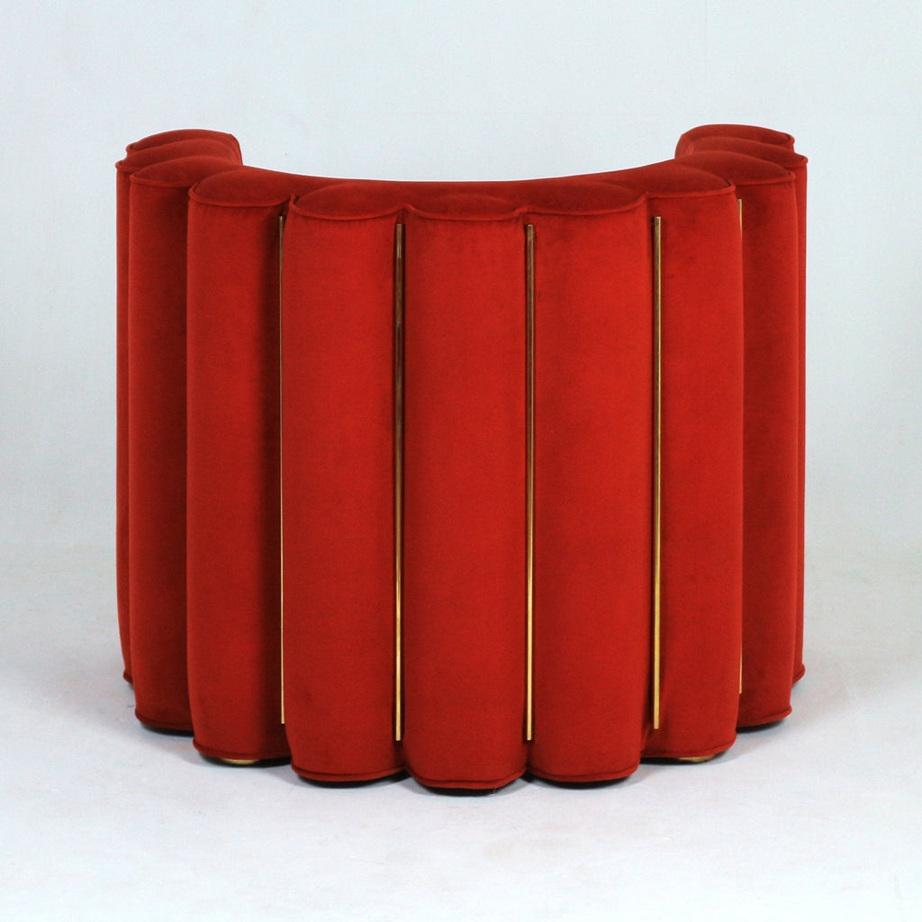 Rear view of a semi-circular modern accent chair upholstered in red velvet with vertical scalloped channels separated by slim gold metal rods, shown against a plain white background.
