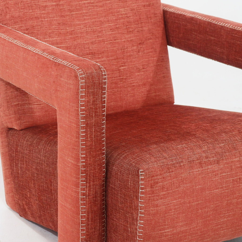 Close-up of a cabernet-red fabric-upholstered modern lounge chair showing the squared arm, cushioned seat and white contrast blanket-stitch detailing along the seams.