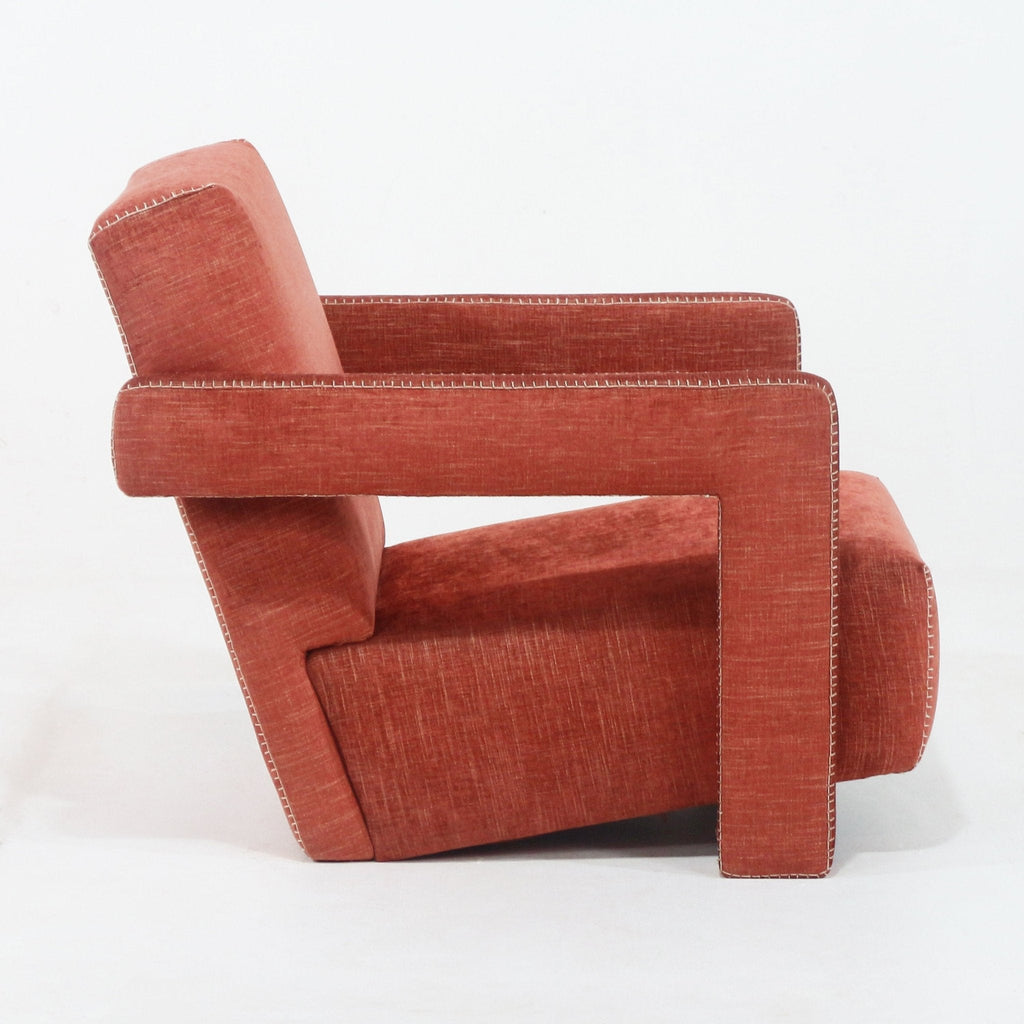 Side profile of a modern fabric-upholstered lounge chair in rust red, featuring a geometric open rectangular arm, full back and visible white contrast topstitching along the edges.