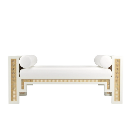 White-painted solid wood bench with natural rattan cane panels, cushioned white fabric seat and two round bolster pillows, boho-contemporary end-of-bed or entryway bench.
