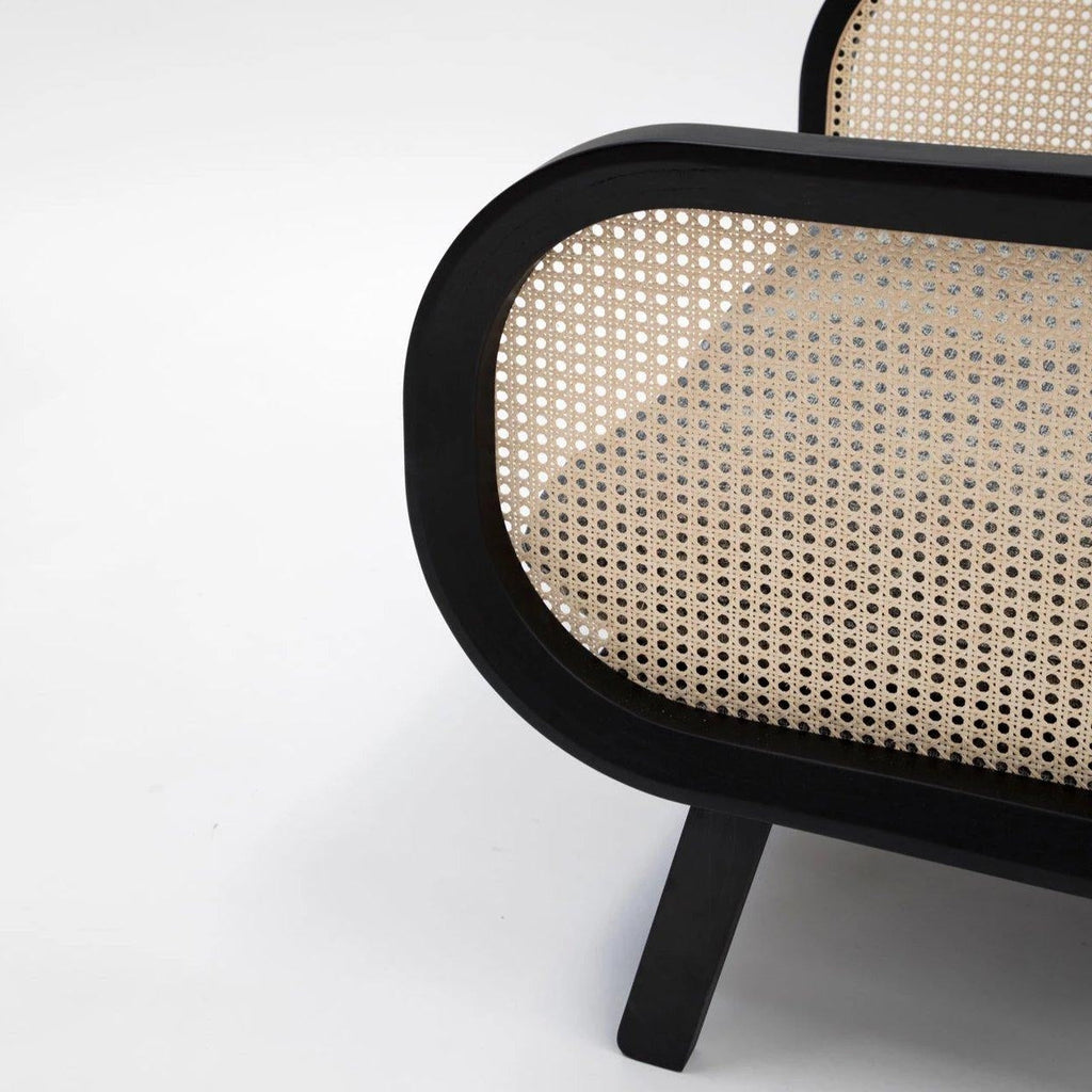 Close-up of a mahogany-black wooden chair frame showing a rounded arm panel with natural woven cane rattan insert and a slanted black leg against a plain white background.