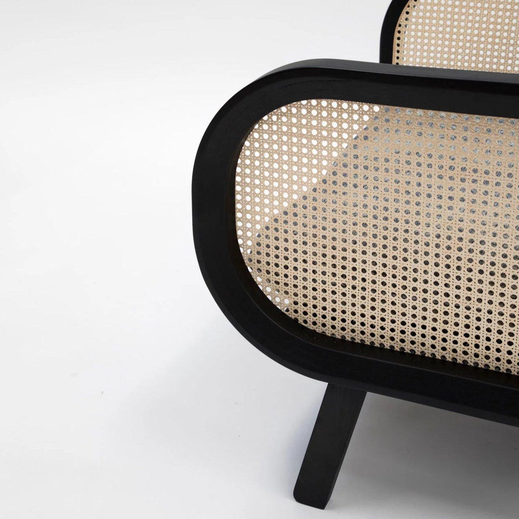 Close-up of a mahogany-black wooden chair frame showing a rounded arm panel with natural woven cane rattan insert and a slanted black leg against a plain white background.