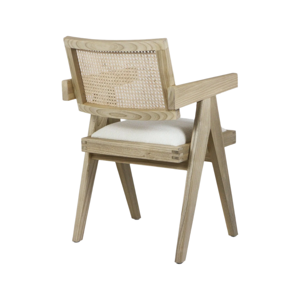 Three-quarter rear view of a natural wood dining armchair with a woven cane back, cream upholstered seat cushion, solid angled legs and straight wooden arms on a white background.