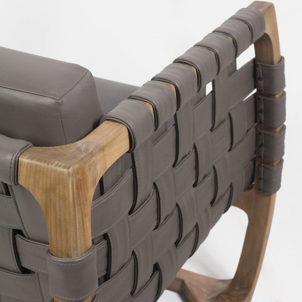 Close-up of a modern lounge chair showing taupe leather straps woven into a webbed back, wrapped and stitched around a natural solid wood frame with a matching taupe cushioned seat.