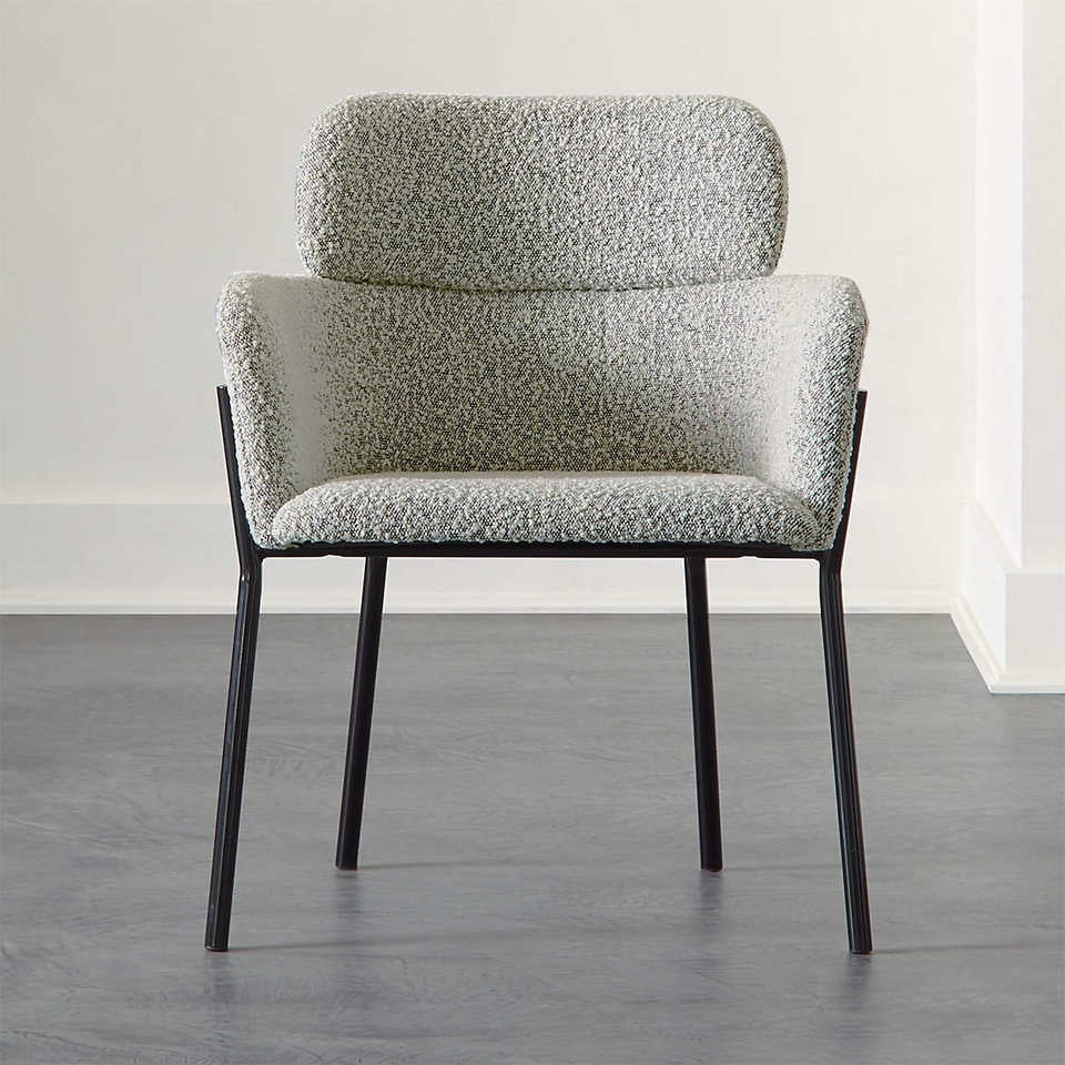 Front-facing grey boucle upholstered dining chair with curved backrest, integrated low arms and a padded headrest detail, set on slim black metal legs against a neutral floor and wall.
