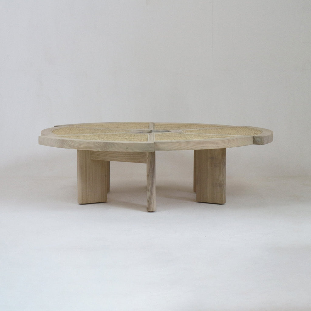 Low round coffee table in natural oak with a woven cane inset top divided into four quadrants and four chunky rectangular legs, shown against a neutral studio background.