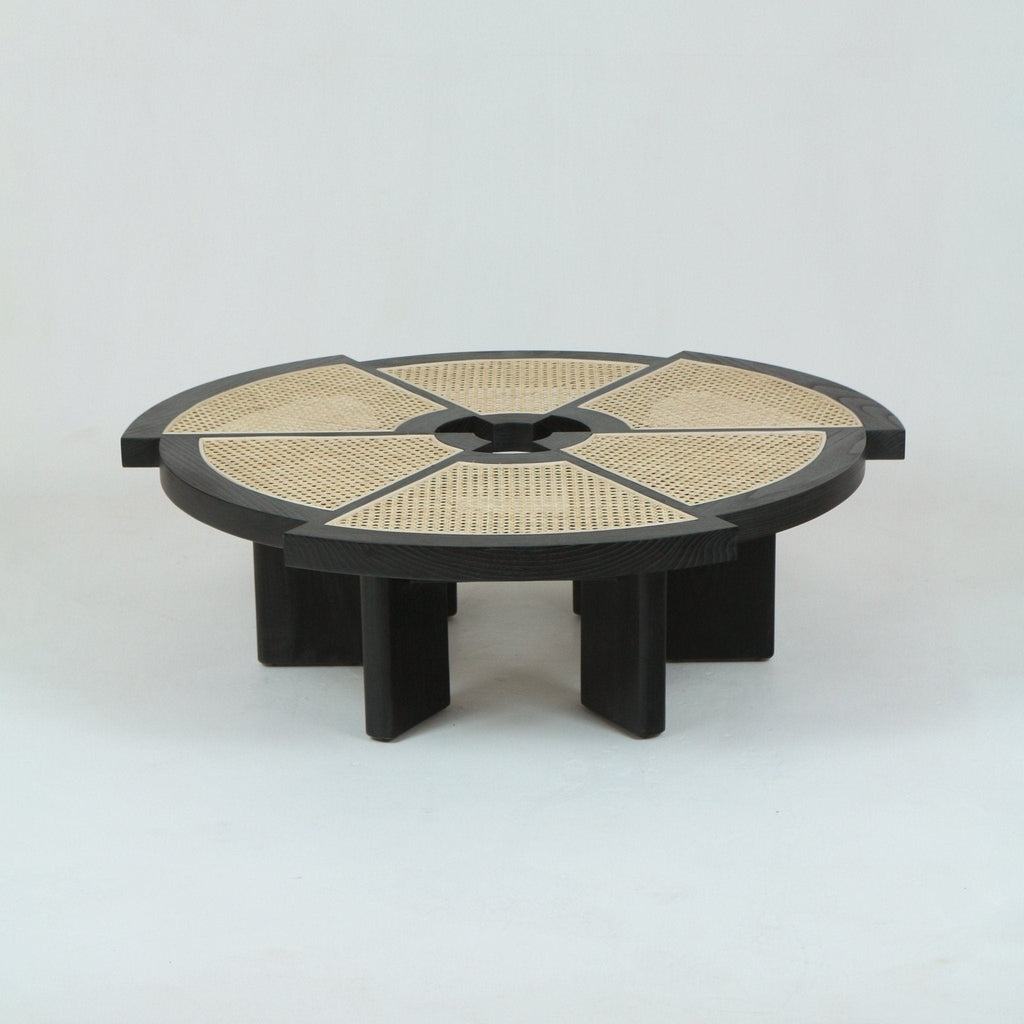 Low round coffee table with a dark solid wood (oak) frame and segmented natural cane insets arranged around a central hub, supported by thick rectangular wood legs for a modern mid-century look.